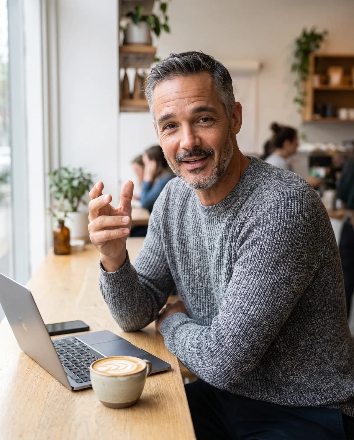 The AI person at a cafe window with a laptop and a coffee, explaining something.