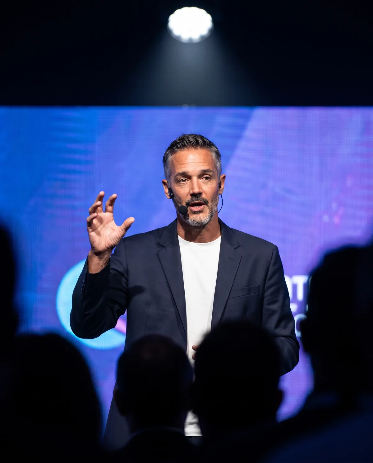The AI person speaking on a conference stage under a spotlight.